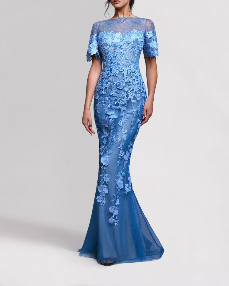 A long blue evening dress featuring lace shoulders, an embroidered guipure bodice and short sleeves, continuing all the way down into a sheer skirt.