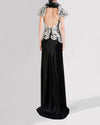 The back of a long black and white evening dress featuring a white beaded bodice, an open back, and puffed short sleeves with delicate lace detailing.