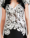 A close-up of a long black and white evening dress featuring a white beaded bodice and puffed short sleeves with delicate lace detailing.