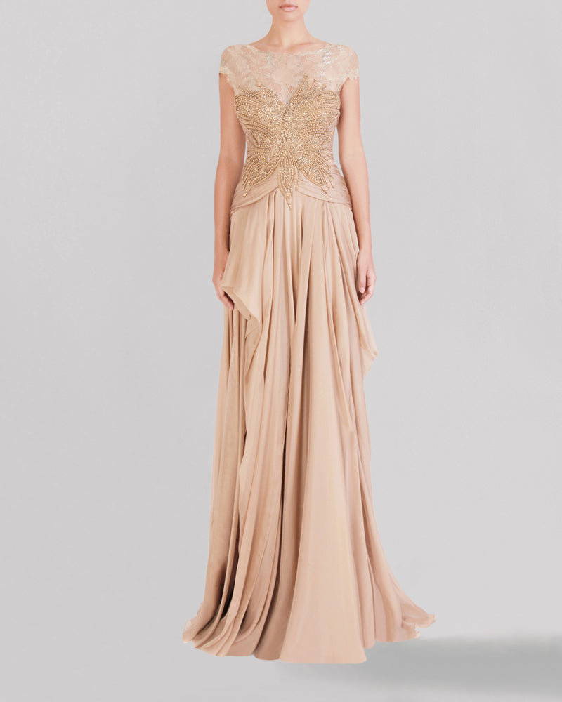 A long beige evening dress featuring a beaded lace bodice, short sleeves, and an asymmetrical gathered skirt.