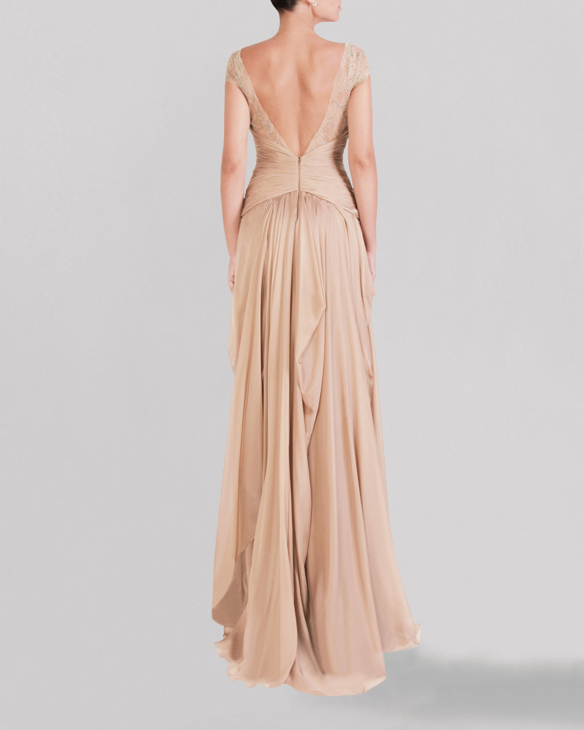 The back of a long beige evening dress featuring a draped lace bodice, short sleeves, an asymmetrical gathered skirt, and a deep V-shape open back.