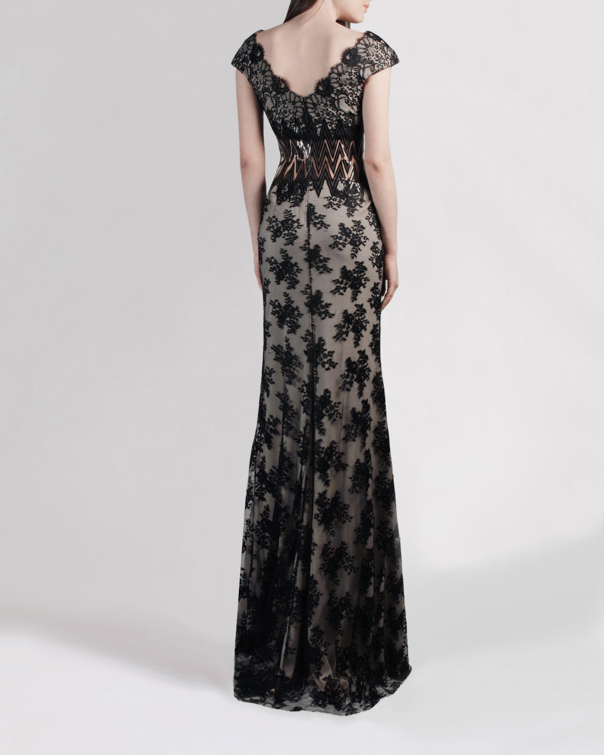 The back of a long black lace evening dress featuring a slight open back with small sleeves and a zigzag see-through waist detailing.