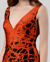 A close-up of a long evening dress in orange and black jacquard fabric featuring a V-neckline and an asymmetrical hemline.