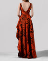 The back of a long evening dress in orange and black jacquard fabric featuring a V-shape open back and an asymmetrical hemline.