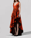 A long evening dress in orange and black jacquard fabric featuring a V-neckline and an asymmetrical hemline.