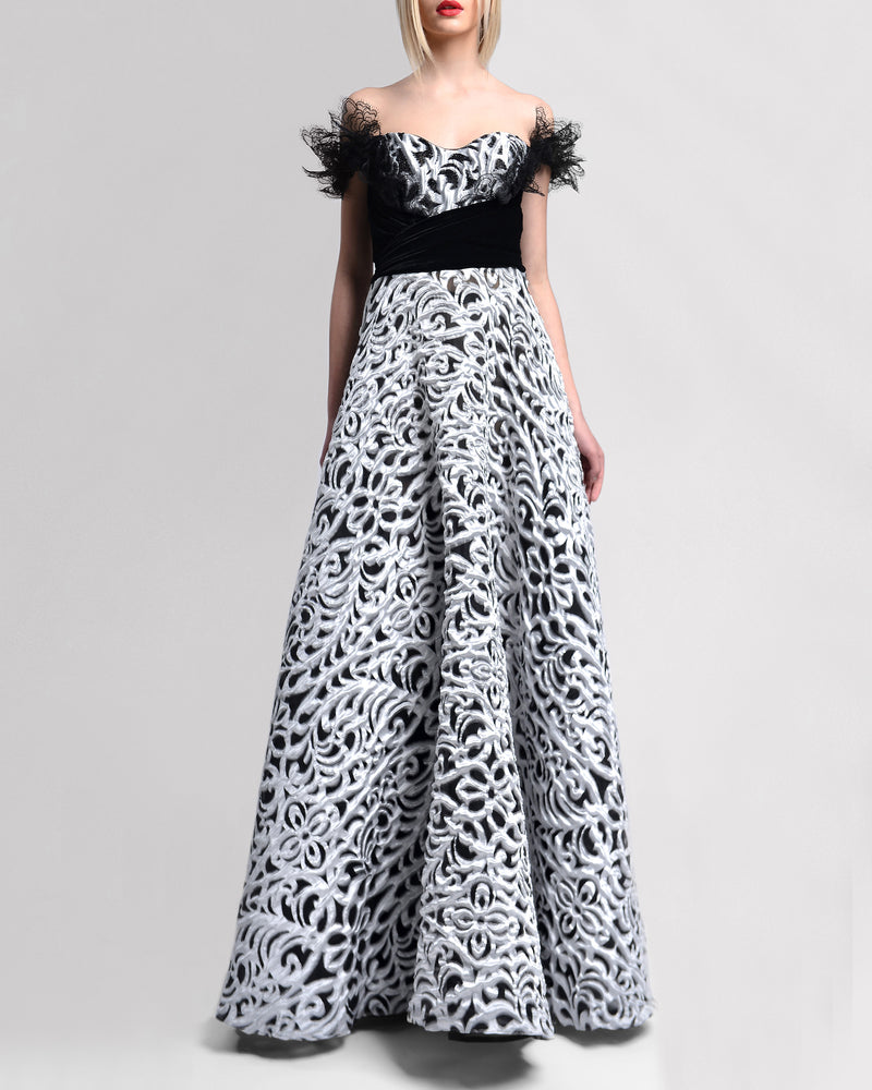 An A-line off-the-shoulders long evening gown with intricate lace sleeve details and a striking black-and-silver contrasting fabric.