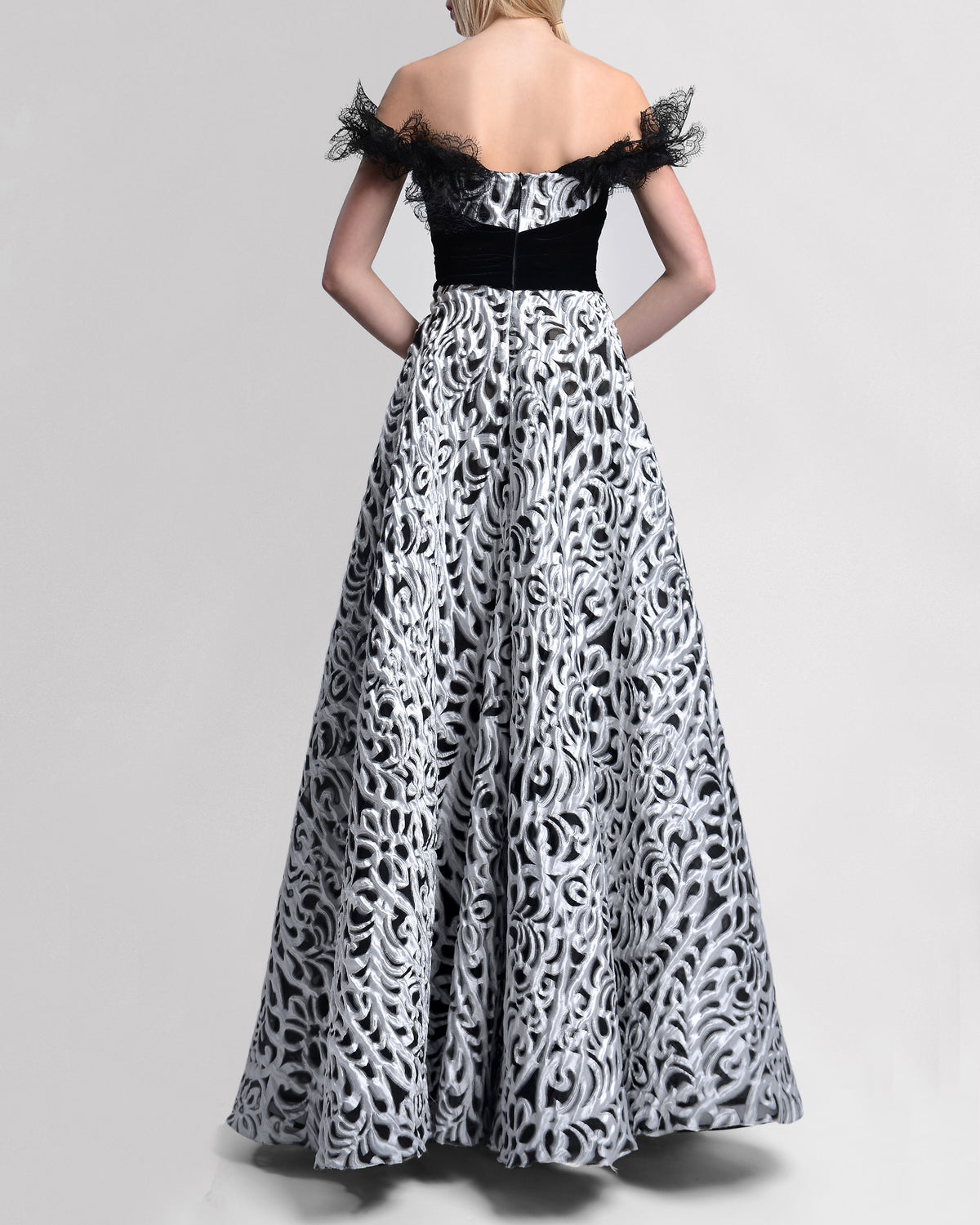 The back of an A-line off-the-shoulders long evening gown with intricate black lace sleeve details and waist, and a striking black-and-silver contrasting fabric.