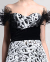 A close-up of an A-line off-the-shoulders long evening gown with intricate lace sleeve details, a draped black velvet waist and a striking black-and-silver contrasting fabric.