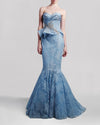 A long blue strapless evening gown featuring a draped bodice, embroidered embellishments, and a mermaid-cut skirt.