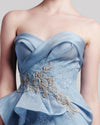 A close-up of a blue strapless evening dress featuring a draped bodice, embroidered embellishments, and a mermaid-cut skirt.