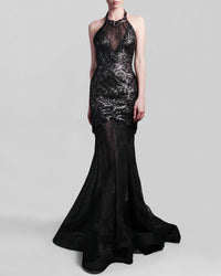 A halter-neck fitted black evening gown in lace and rose patterned sequins fabric, and a sheer floor-length skirt with a flowing train.