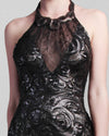 A close-up of a halter-neck fitted black evening gown in lace and patterned sequin fabric.