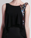 A close-up of a black evening dress with a chiffon overlay, featuring beading details on one shoulder.