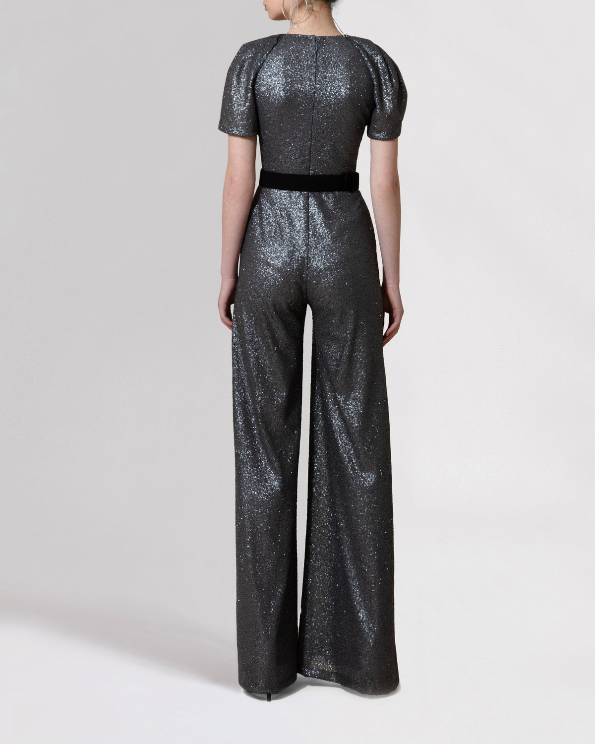 The back of a dark grey jumpsuit featuring short puffed sleeves, a deep V-neckline and wide legs paired with a black belt.