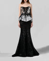 An evening wear style featuring a strapless sliver top with black lace embellishments paired with a long black mermaid cut skirt in a shimmery mesh fabric.